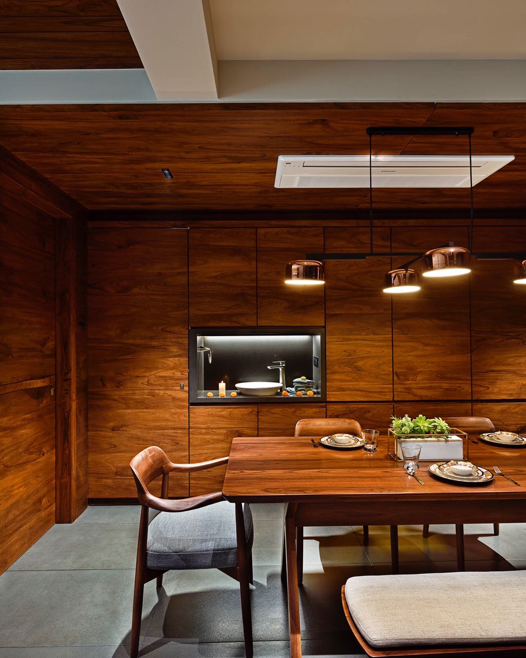 MA HOME dining table set for a meal against full-height teak panelling with a lit niche