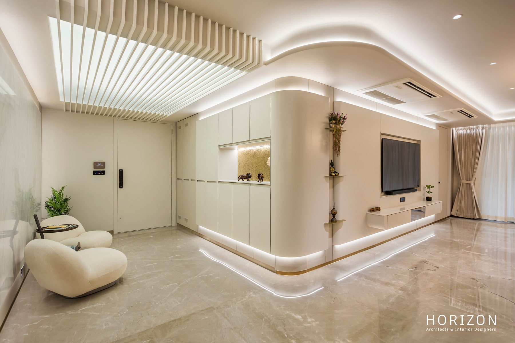 RAHUL BHAI HOME living room seen from the foyer: curved cove-lit TV wall, boucle lounge chair and potted plant