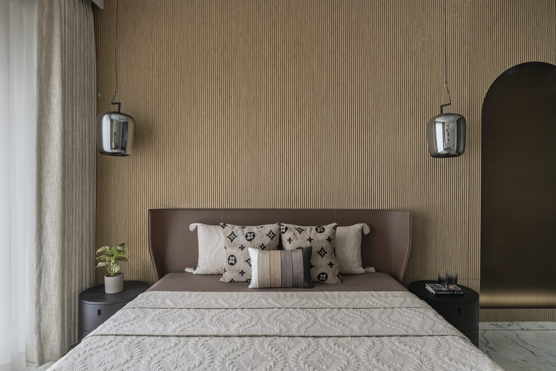 SACHIN BHAI HOME primary bedroom with fluted timber wall, twin chrome pendants and brass arch niche