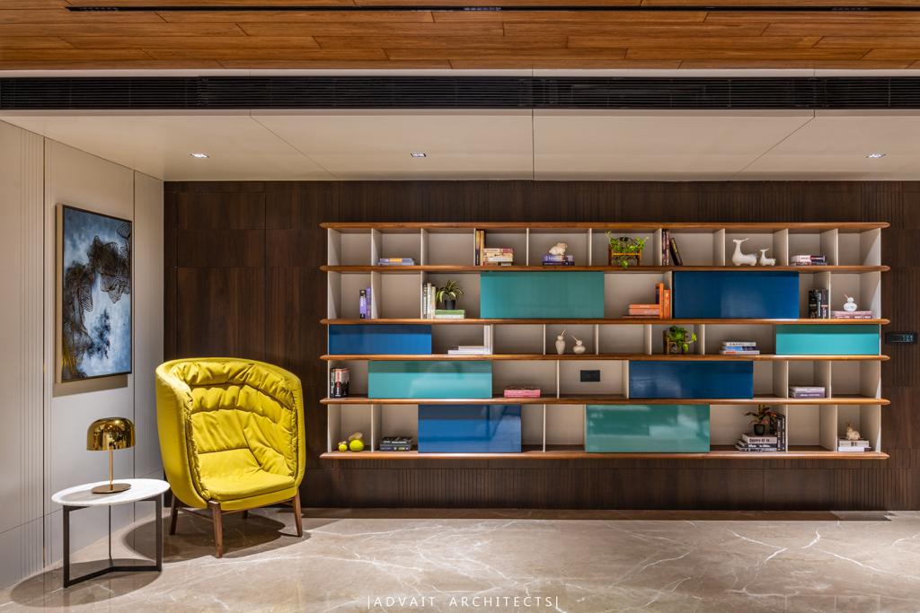 VILLASHBHAI HOME library wall of open shelving in teal and timber with a yellow armchair